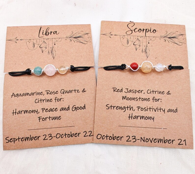 May include: Two handmade Libra and Scorpio zodiac bracelets. The Libra bracelet features aquamarine, rose quartz, and citrine beads. The Scorpio bracelet features red jasper, citrine, and moonstone beads. Each bracelet is on a black cord.
