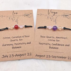 May include: Two handmade gemstone bracelets on display. One features citrine, carnelian, and rose quartz, while the other showcases rose quartz, amethyst, and citrine. Each bracelet is on a card with the zodiac sign and associated traits.