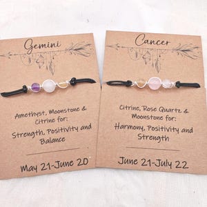 May include: Two beaded bracelets with black cords, displayed on brown cards. One card reads "Gemini" and the other "Cancer." The Gemini bracelet features amethyst, moonstone, and citrine. The Cancer bracelet features citrine, rose quartz, and moonstone.