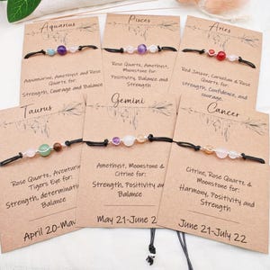 May include: Zodiac sign bracelets with gemstone beads on black cords. Each bracelet is displayed on a card with the zodiac sign and associated gemstones like amethyst, rose quartz, and citrine. The cards also list the properties of the gemstones.