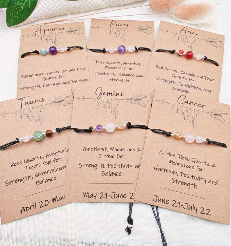May include: Zodiac sign bracelets with gemstone beads on black cords. Each bracelet is displayed on a card with the zodiac sign and associated gemstones like amethyst, rose quartz, and citrine. The cards also list the properties of the gemstones.