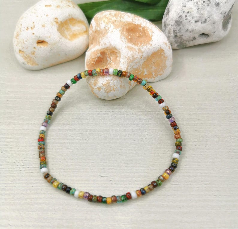 May include: A colorful beaded bracelet featuring a variety of small, round beads in shades of red, green, yellow, blue, and white. The bracelet is strung on a flexible cord and is approximately 7 inches in length.