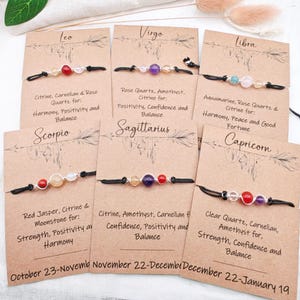 May include: A collection of gemstone bracelets displayed on individual cards. Each bracelet features a different combination of stones, such as citrine, amethyst, and rose quartz, strung on a black cord. The cards include zodiac signs and descriptions.