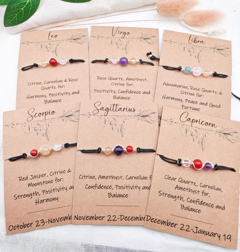May include: A collection of gemstone bracelets displayed on individual cards. Each bracelet features a different combination of stones, such as citrine, amethyst, and rose quartz, strung on a black cord. The cards include zodiac signs and descriptions.