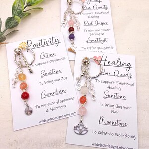 Pu&ograve; includere: Portachiavi con perline di pietre preziose e ciondoli color argento. Ogni portachiavi ha un tema diverso: Positivit&agrave;, Dolore e Guarigione. Le carte includono i nomi delle pietre preziose e le loro propriet&agrave;. Il sito web wildejadedesigns.etsy.com &egrave; stampato.
