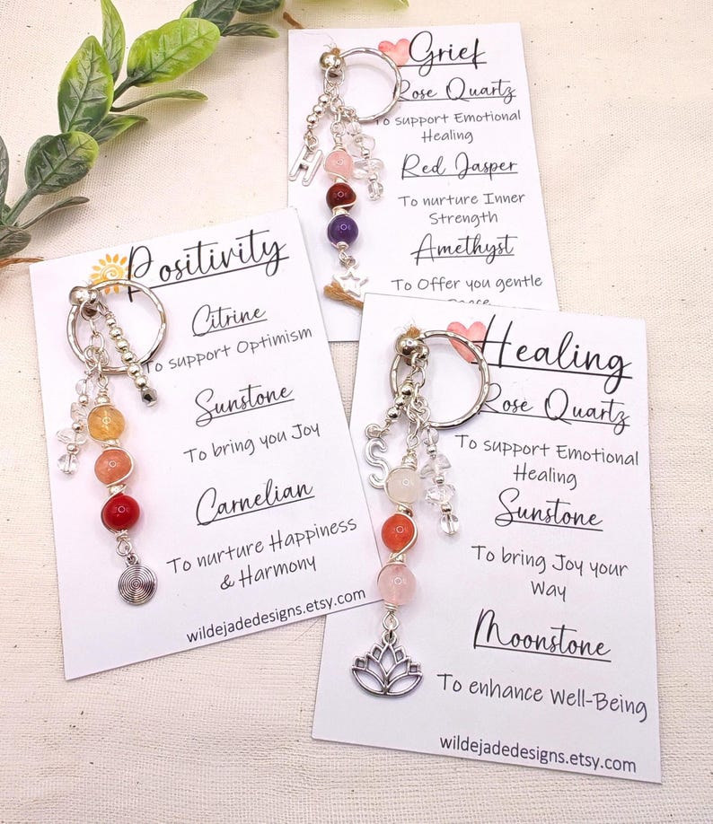 Pu&ograve; includere: Portachiavi con perline di pietre preziose e ciondoli color argento. Ogni portachiavi ha un tema diverso: Positivit&agrave;, Dolore e Guarigione. Le carte includono i nomi delle pietre preziose e le loro propriet&agrave;. Il sito web wildejadedesigns.etsy.com &egrave; stampato.