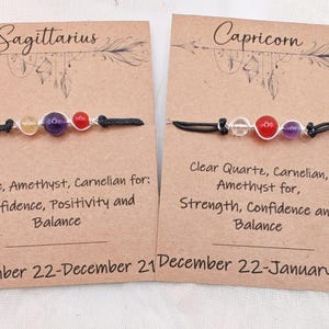 May include: Two gemstone bracelets on cards. One reads "Sagittarius" with citrine, amethyst, and carnelian beads. The other reads "Capricorn" with clear quartz, carnelian, and amethyst beads. Each card has text about the stones' properties.