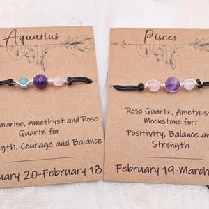 May include: Two bracelets with gemstone beads on black cords, displayed on brown cards. One features aquamarine, amethyst, and rose quartz; the other, rose quartz, amethyst, and moonstone. Text on the cards indicates zodiac signs and associated qualities.