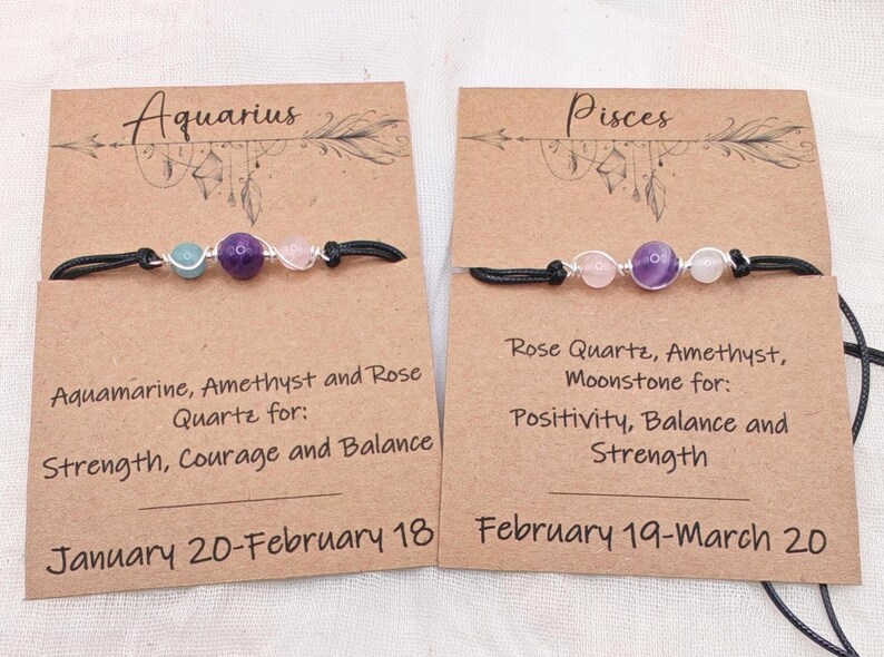 May include: Two bracelets with gemstone beads on black cords, displayed on brown cards. One features aquamarine, amethyst, and rose quartz; the other, rose quartz, amethyst, and moonstone. Text on the cards indicates zodiac signs and associated qualities.