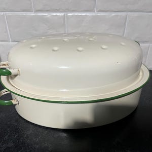 May include: White enamel oval baking dish with a green rim and a matching lid. The lid has small holes for steam release.