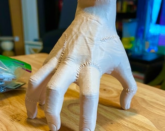 Puede incluir: Una mano blanca impresa en 3D con costuras. La mano está en posición con los dedos extendidos y ligeramente curvados.