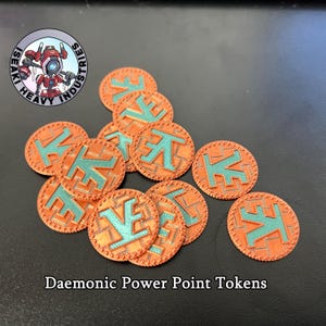 Puede incluir: Fichas de puntos de poder demoníacos naranjas y turquesas. Cada ficha presenta un diseño de letra turquesa sobre un fondo naranja con un borde texturizado. Las fichas están dispersas sobre una superficie oscura.