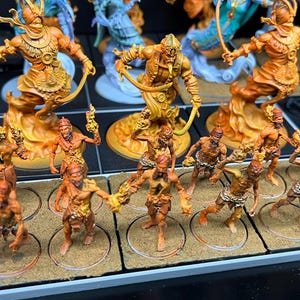 May include: Miniature figurines of fantasy characters, painted in shades of orange and brown. The figures include warriors with swords and other weapons, and are arranged on a display surface. The overall theme is likely for tabletop gaming or collecting.