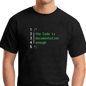 May include: Black t-shirt with green text: "1 /* 2 | the Code is 3 documentation 4 | enough 5 */". The text is vertically aligned on the front. The shirt has a crew neck.