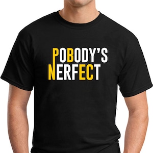 May include: Black t-shirt featuring the text "POBODY'S NERFECT" in white and yellow. The crew neck shirt is made of a soft material. The text is a humorous play on words.