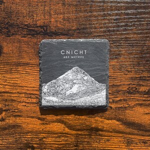 May include: A black slate coaster with a white illustration of a mountain and the text "CNICHT 689 METRES".