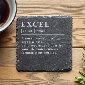 Könnte beinhalten: Ein quadratischer, dunkelgrauer Schieferuntersetzer mit der Definition von "EXCEL" in weißem Text. Die Definition beschreibt Excel humorvoll als Arbeitsplatzwerkzeug. Eine Tasse Kaffee befindet sich links, Kiefernnadeln rechts.