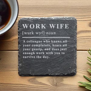 Könnte beinhalten: Ein quadratischer, dunkelgrauer Schieferuntersetzer mit dem Text "WORK WIFE" und einer Definition in Weiß. Der Untersetzer liegt auf einer Holzoberfläche neben einer Kaffeetasse und Kiefernnadeln.