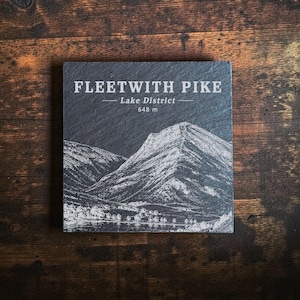 May include: A square dark grey slate coaster featuring a white laser-etched illustration of Fleetwith Pike in the Lake District. The text reads FLEETWITH PIKE, Lake District, and 648 m. The surface has a natural, textured, and matte finish.
