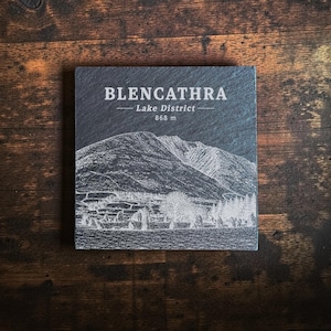 May include: A square dark grey slate coaster featuring a white laser-engraved illustration of the Blencathra mountain in the Lake District. The text reads BLENCATHRA, Lake District, and 868 m, centred above the mountain landscape graphic.