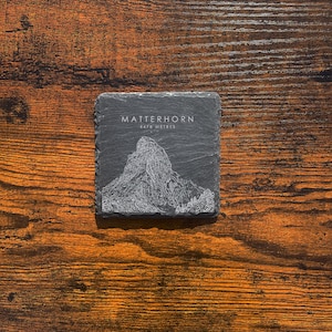 May include: A black slate coaster featuring a white line drawing of the Matterhorn mountain and the text "Matterhorn 4478 metres".