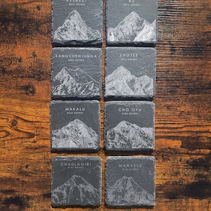 以下が含まれることがあります： 世界で最も高い山々、エベレスト、K2、カンチェンジュンガ、ロツェ、マカルー、チョ・オユー、ダウラギリ、マナスルを描いた、黒いスレート製のコースター8枚セット。各コースターには、山の名前と標高がメートル単位で記載されています。