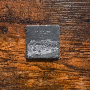 May include: A black slate coaster with a white line drawing of a mountain range and the text "LA PLAGNE FRANCE".