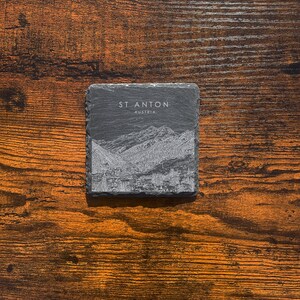 May include: A black slate coaster with a white etched image of mountains and the text "St. Anton Austria".