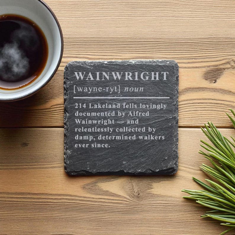 May include: A square, dark gray slate coaster with the name "WAINWRIGHT" in white text. The coaster also features a definition and a description of the word. A cup of coffee and pine needles are in the background.