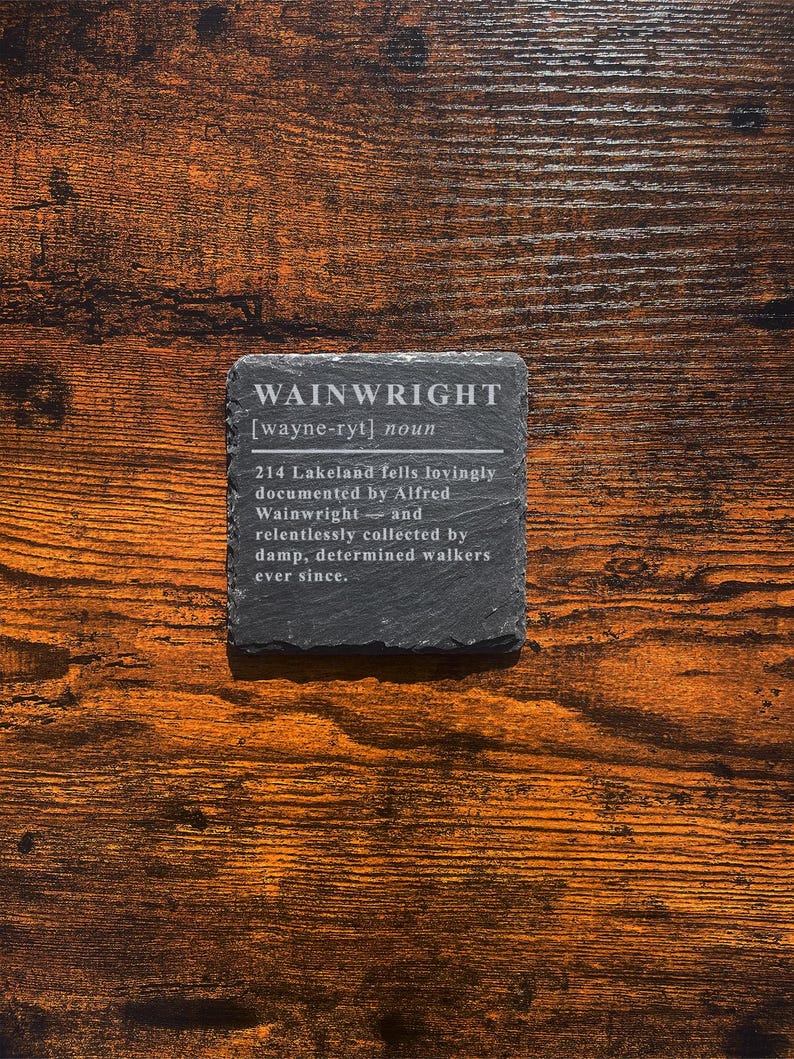 May include: A square, dark gray slate coaster with the word "WAINWRIGHT" and its pronunciation etched in white. The coaster also includes a definition and description. The coaster sits on a wooden surface.