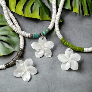 Peut inclure: Trois colliers de perles blanches avec des pendentifs en forme de fleur. Les colliers ont des perles blanches, avec des sections de perles turquoise, marron et vertes. Les pendentifs en forme de fleur sont blancs et ont un design de pétales détaillé.
