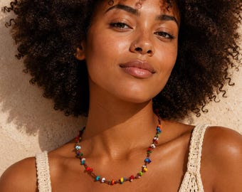 May include: A delicate necklace featuring a thin brown cord adorned with small, multi-colored beads in shades of red, blue, yellow, green, and white, worn with a beige sleeveless top featuring a textured, open-knit crochet pattern.
