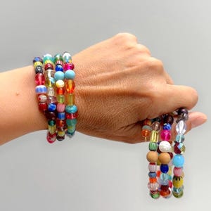 May include: A collection of colourful beaded bracelets. The bracelets are made up of beads in a variety of shapes and sizes, including round, cylindrical, and irregular. The beads are in shades of red, blue, yellow, and green.