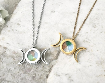 May include: Two necklaces with a celestial design. One is silver-toned, the other gold-toned. Each features a pendant with a circular glass compartment filled with colorful stones, framed by crescent moon shapes. The necklaces hang on delicate chains.