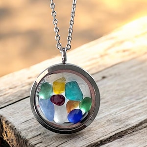 May include: A silver-toned necklace with a round pendant filled with colorful, polished stones. The stones are various colors, including blue, green, yellow, and red. The pendant hangs from a delicate chain, creating a simple yet eye-catching accessory.