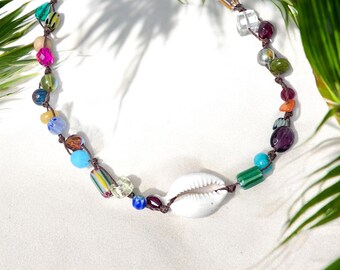 May include: A colorful necklace featuring a white seashell pendant and an assortment of beads in various shapes and colors, including pink, green, blue, and clear. The beads are strung on a brown cord.