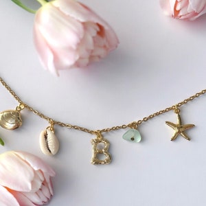 May include: Gold-tone necklace with seashell, starfish, and letter "B" charms. The necklace also features a small piece of sea glass. The chain is delicate and the charms are detailed.