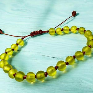 May include: A beaded bracelet featuring translucent, chartreuse-colored beads strung on a brown cord. The bracelet has an adjustable sliding knot closure. The beads are round and evenly spaced, creating a simple, elegant design.