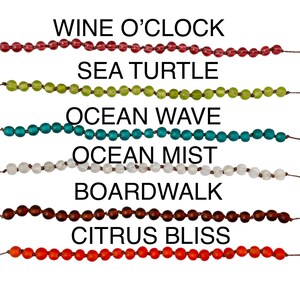 May include: A collection of beaded bracelets in various colors, including red, green, teal, white, brown, and orange. Each bracelet is labeled with a descriptive name such as "Wine O'Clock" and "Citrus Bliss".