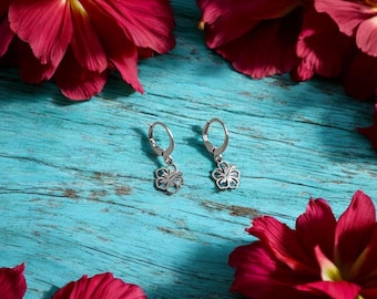 May include: A pair of silver-colored flower-shaped earrings with a lever back closure. The earrings are displayed on a turquoise wooden surface, surrounded by vibrant red flower petals.