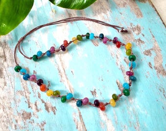 May include: A colorful beaded necklace with a brown cord. The necklace features a variety of small, round beads in shades of red, orange, yellow, green, blue, and purple. The beads are strung together on a brown cord.
