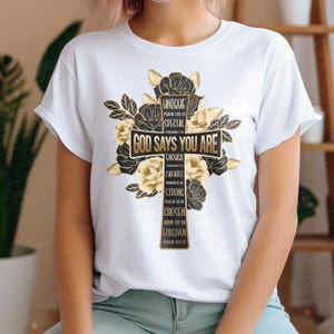 May include: White t-shirt with a black cross design surrounded by gold flowers. The cross has the words "God Says You Are" and a list of positive affirmations with bible verses.
