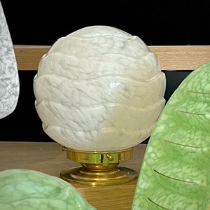 May include: A white glass lampshade with a textured, wavy design sits on a brass base. The lampshade is round and has a frosted finish.