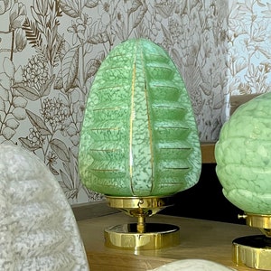 May include: Two green glass table lamps with gold accents. The lamps have a textured, ribbed design and are on a wooden surface.