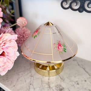 May include: A white lampshade with a gold trim and floral design. The lampshade is on a gold base.
