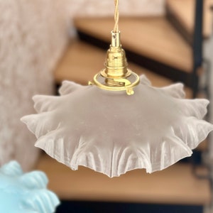 May include: A white frosted glass lampshade with a ruffled edge hangs from a gold metal pendant light fixture.