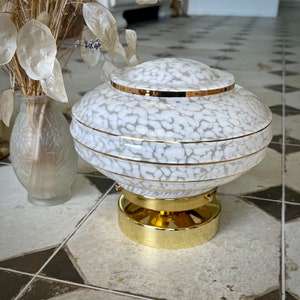 May include: A white and gold ceiling lamp with a decorative, patterned design. The lamp has a round, layered shade with a gold base.