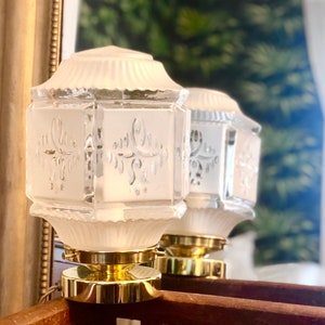 May include: Two frosted glass lamps with gold bases. The lamps have a geometric design and are decorated with etched floral patterns.