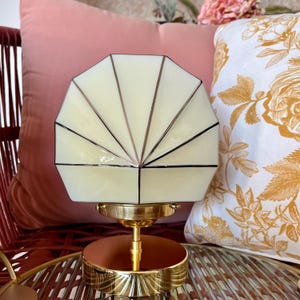 May include: A decorative lamp with a geometric, off-white shade featuring black lines and a brass base. The lamp has a circular base with a copper-colored top. The lamp is a stylish home decor item.