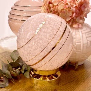 May include: A pink glass globe lamp with gold stripes and a gold base. The globe has a white marbled pattern.